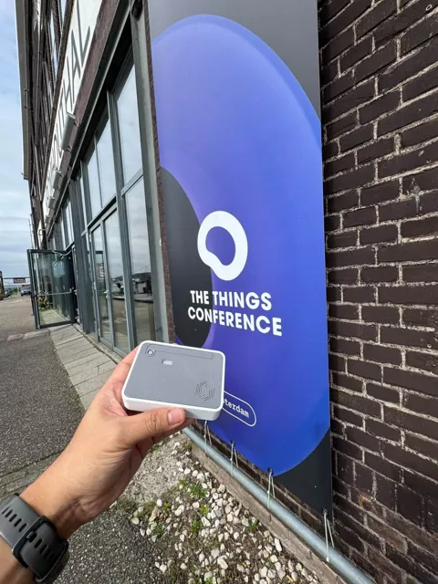 A Cubicore team member holding a LoRaWAN device in front of a The Things Conference banner
